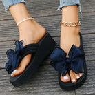 Women's black platform sandals with large navy bows, worn with anklets and jeans. Fashionable summer footwear, stylish casual look.