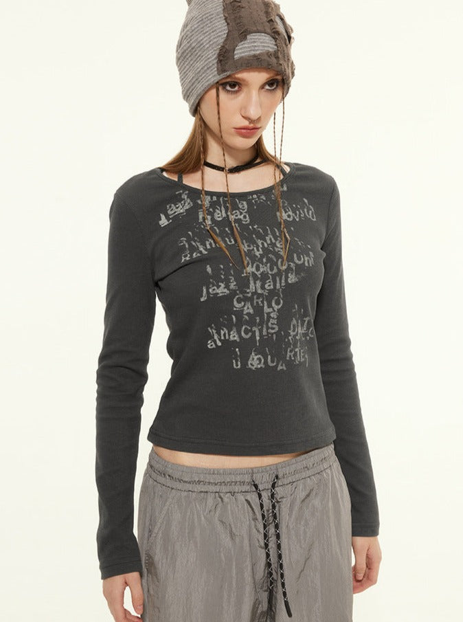 Woman in a stylish gray long-sleeve top with abstract text design, wearing a knit beanie and gray drawstring pants. Fashionable casual outfit.