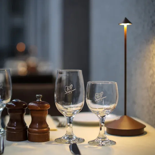 Elegant dining table setup with two wine glasses, salt and pepper shakers, and a modern table lamp. Perfect for upscale restaurant ambiance.