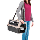 Woman carrying a portable pet carrier with shoulder strap, featuring a secure latch door and ventilation slots, ideal for small dogs or cats.