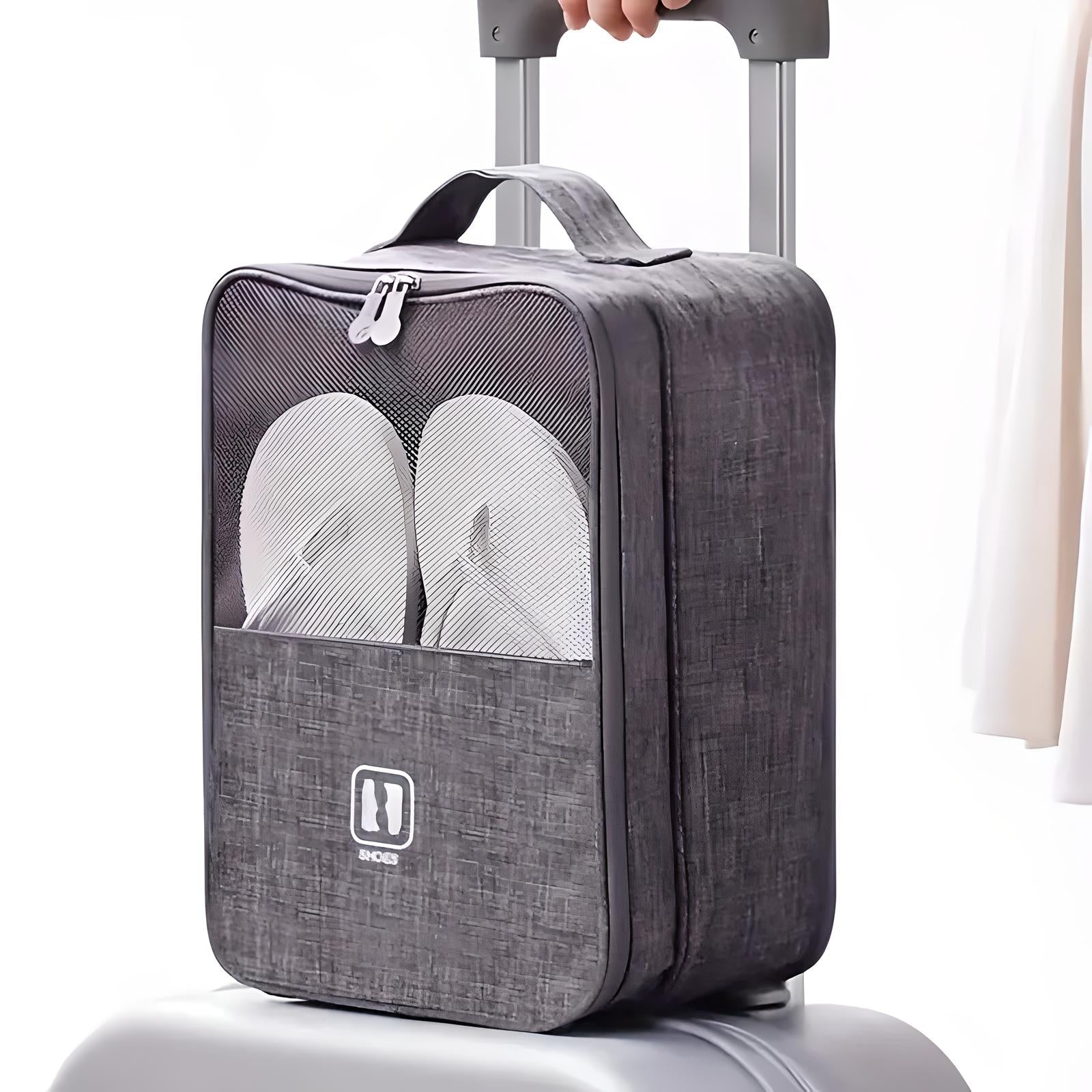 Travel shoe bag with handle, gray fabric, transparent front pocket displaying white flip-flops, placed on a suitcase handle. Ideal for organized packing.