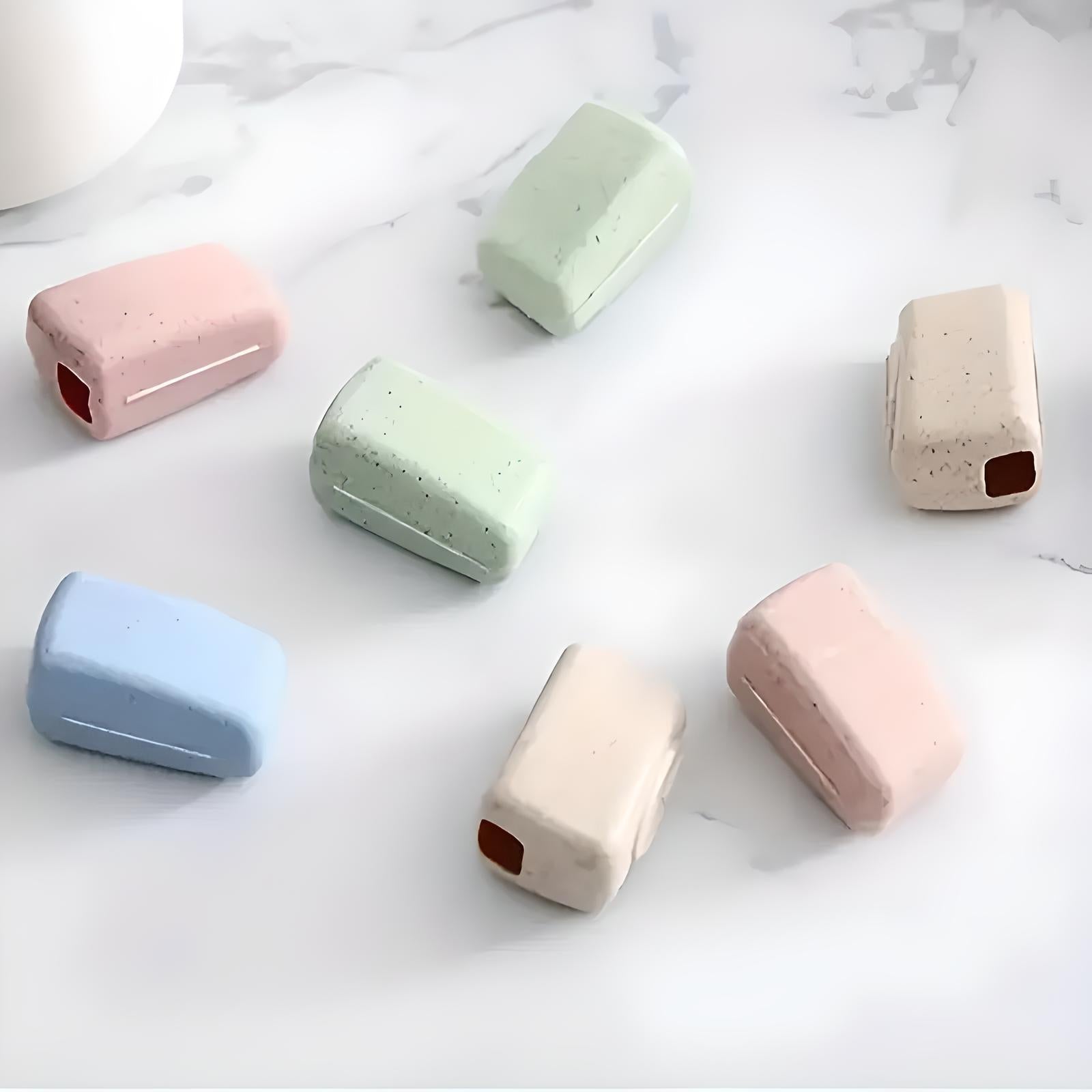 Colorful ceramic toothbrush holders on a marble surface, featuring pastel shades of pink, blue, green, and beige. Modern bathroom accessories.