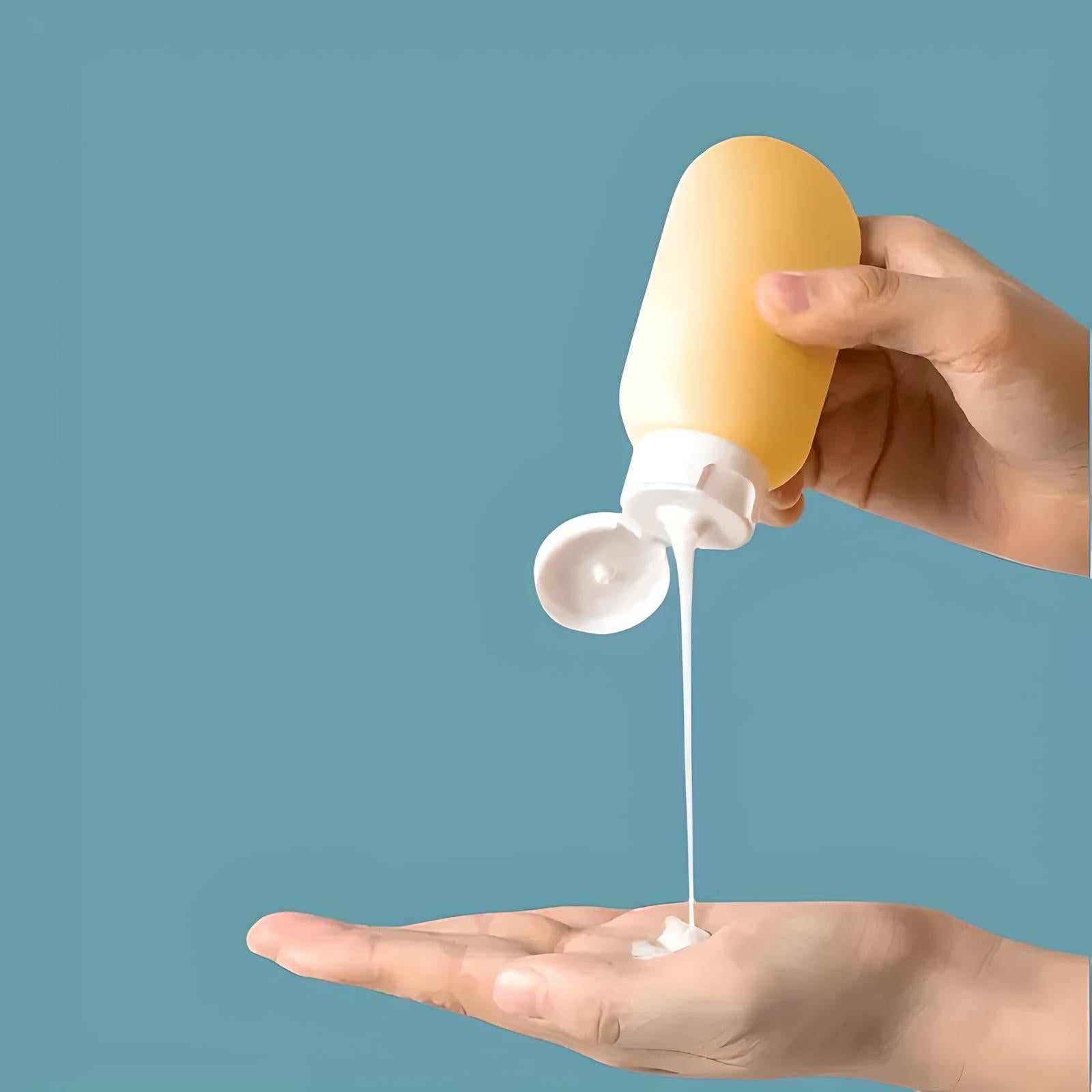 Hand pouring lotion from a yellow bottle onto palm against a blue background. Skincare, moisturizing, personal care product.