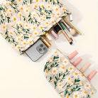 Floral makeup bag with daisy pattern, containing cosmetics, brushes, and a smartphone. Beauty essentials, travel pouch, stylish accessory.