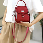 Woman holding a stylish red crossbody bag with silver accents, wearing a white top and beige pants. Fashionable accessory for casual outfits.