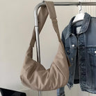 Beige shoulder bag on a metal rack next to a denim jacket; stylish fashion accessory, casual outfit, modern design, versatile handbag.