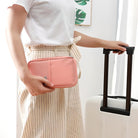 Woman holding a pink travel wallet next to a white suitcase with black handle, wearing a white shirt and striped skirt. Travel accessories, luggage.