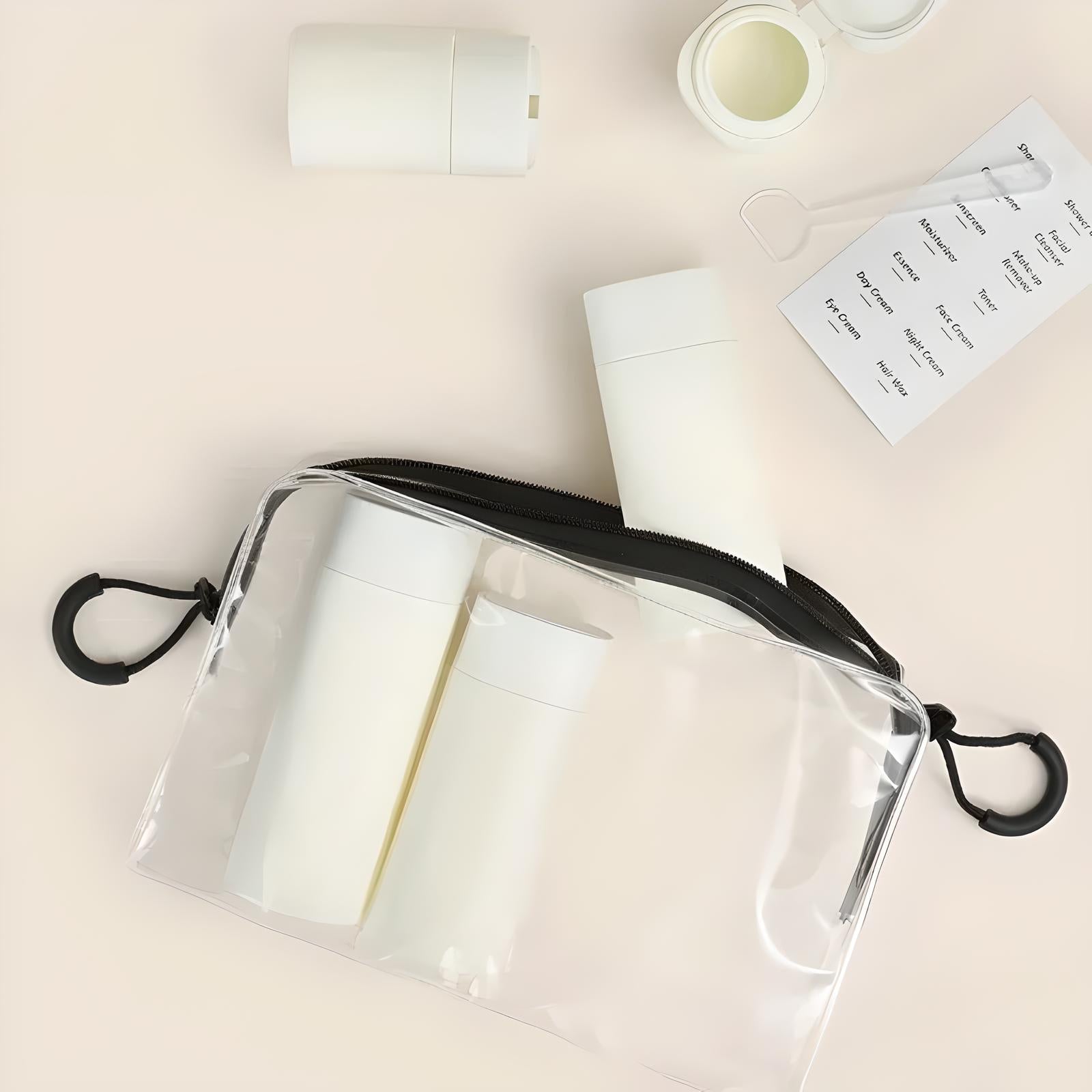 Clear travel toiletry bag with white bottles, labels, and a spatula on a beige background. Ideal for organizing skincare products.