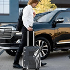 Man with sleek black suitcase near luxury SUV, wearing formal attire. Travel, business trip, stylish luggage, modern transportation.