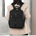 Woman wearing a stylish black backpack with multiple zippered compartments, ideal for travel and work, against a modern indoor background.