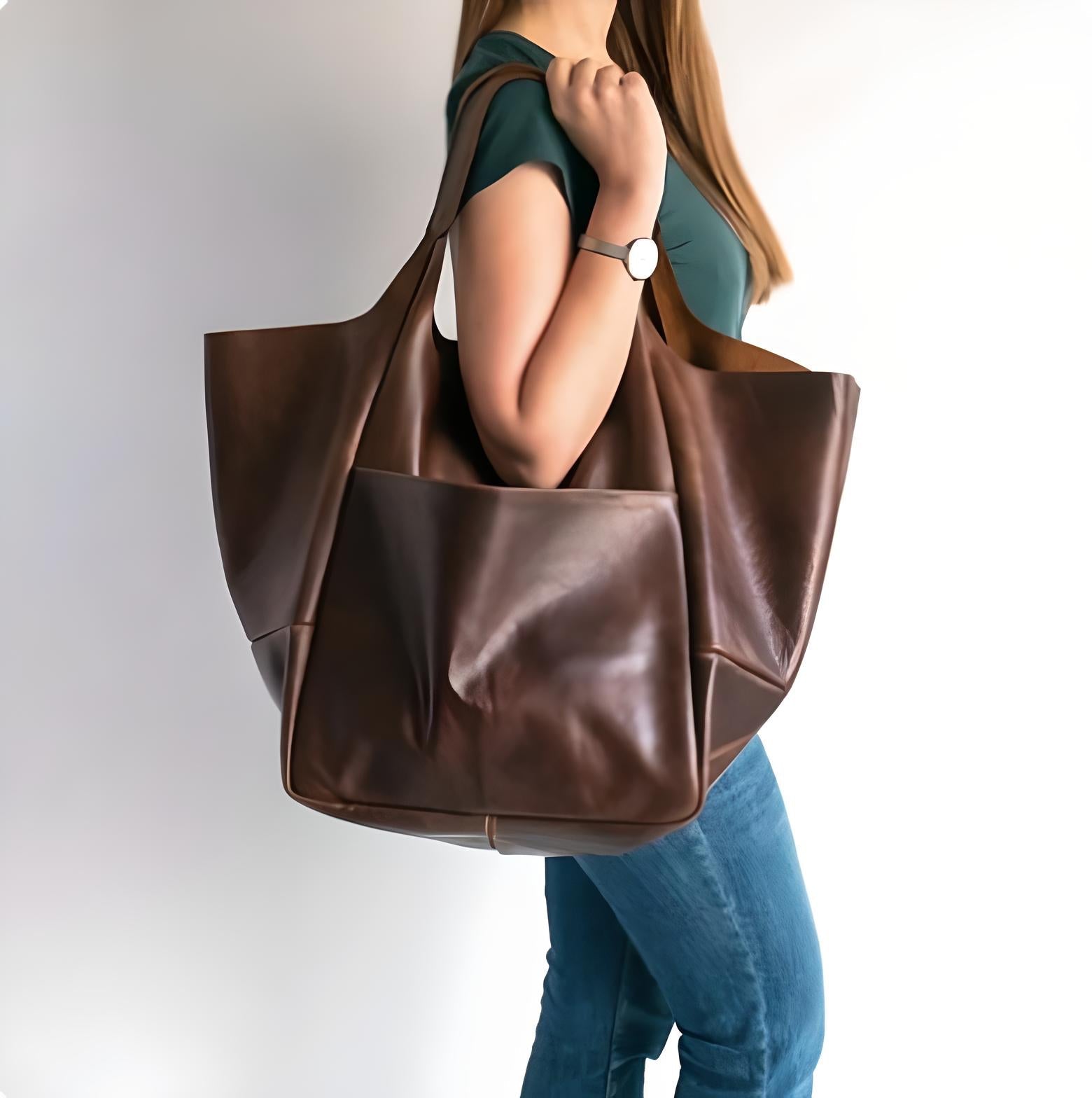 Woman carrying oversized brown leather tote bag, wearing casual green top and jeans. Fashion accessory, stylish handbag, everyday carry.