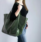 Woman carrying large green leather tote bag, wearing black top and jeans. Fashionable accessory, stylish handbag, casual outfit.