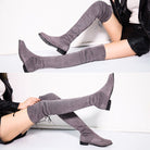 Gray over-the-knee suede boots with block heels, worn by a seated person in black shorts and a leather jacket, showcasing stylish fall footwear.