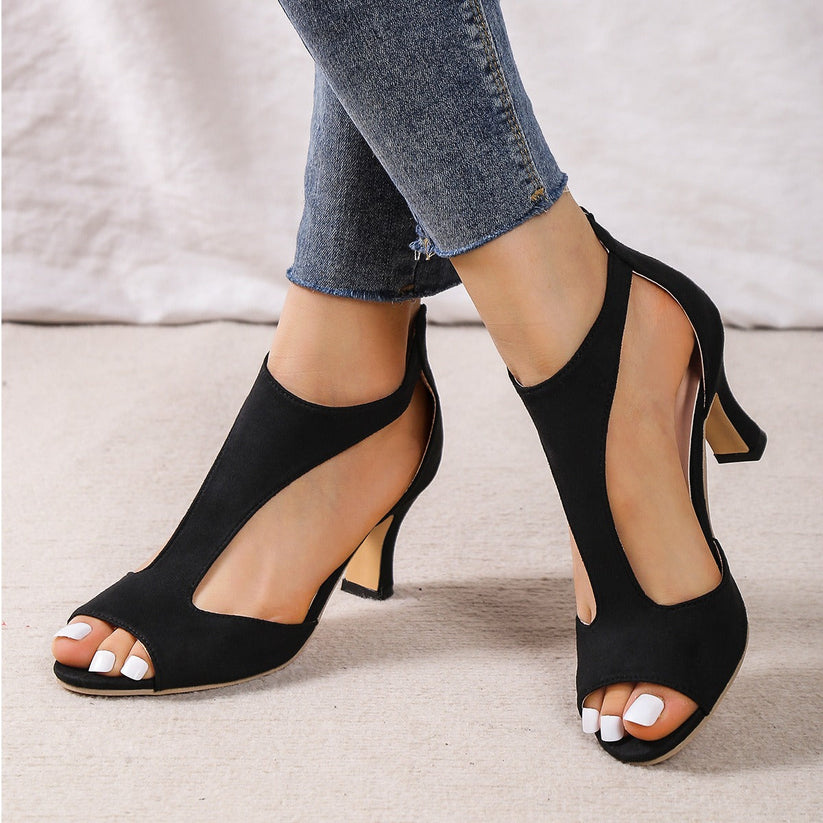 Black open-toe high heel sandals with cutout design, worn with blue jeans. Stylish summer footwear for women, perfect for casual or formal occasions.