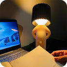 Modern table lamp with unique design, soft ambient lighting next to an open laptop and book, perfect for cozy home office or study setup.