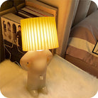 Quirky human-shaped table lamp with pleated shade on a cozy bedside table, modern home decor, warm ambient lighting, unique bedroom accessory.