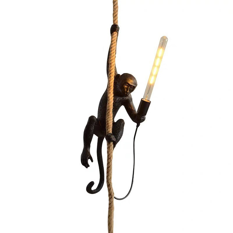 Monkey lamp hanging on rope, holding LED bulb. Unique home decor, creative lighting fixture, black monkey design, modern interior accessory.