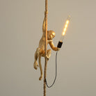 Gold monkey lamp hanging on a rope, holding an illuminated LED bulb. Unique home decor, modern lighting fixture, artistic design, ambient light.