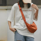 Woman wearing oversized white t-shirt with "Bread and Butter column" text, paired with denim shorts and an orange crossbody bag, casual streetwear fashion.