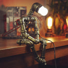 Industrial pipe lamp shaped like a sitting figure on a wooden table, emitting warm light. Unique steampunk decor, vintage lighting design.