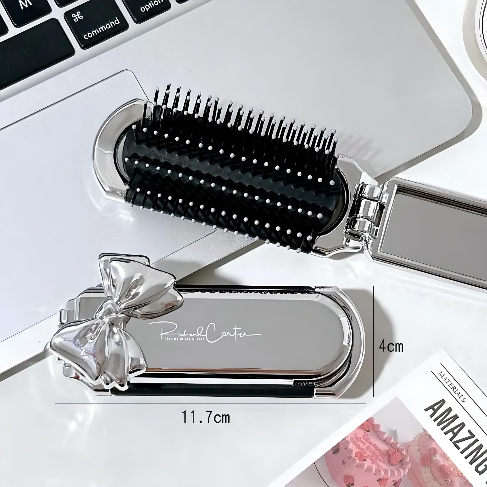 Compact silver hairbrush with a bow design, measuring 11.7cm by 4cm, placed on a laptop. Ideal for travel, stylish grooming accessory.