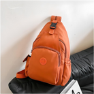 Orange sling backpack with multiple compartments, adjustable strap, and side pocket, placed on a black sofa. Stylish and functional travel bag.