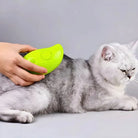 Person using a green pet grooming tool on a relaxed gray cat. Cat grooming, pet care, fur maintenance, handheld pet brush, feline hygiene.