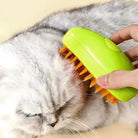 Person using a green pet grooming brush on a fluffy gray cat. Cat grooming tool, pet care, fur maintenance, and shedding control.