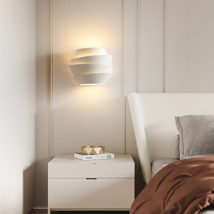 Modern white wall sconce illuminating a minimalist bedroom with beige walls, featuring a sleek nightstand and cozy bedding. Contemporary lighting decor.