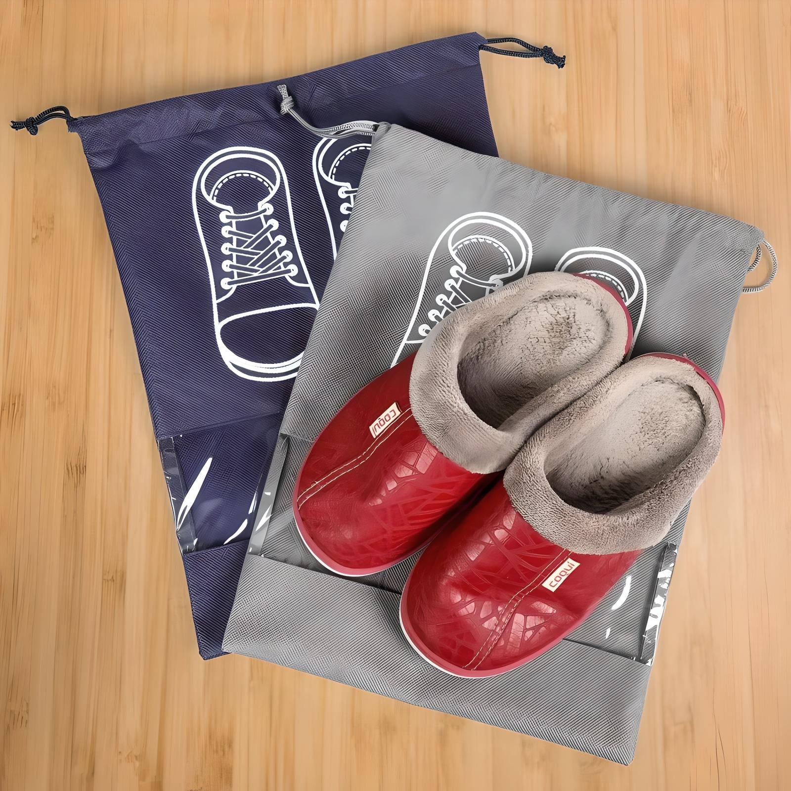 Red winter slippers with plush lining on a wooden floor, accompanied by two drawstring shoe bags featuring sneaker illustrations. Cozy footwear storage solution.