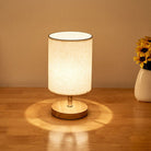 Modern table lamp with beige fabric shade on wooden base, illuminating a warm glow. Ideal for bedroom or living room decor. Cozy lighting accessory.