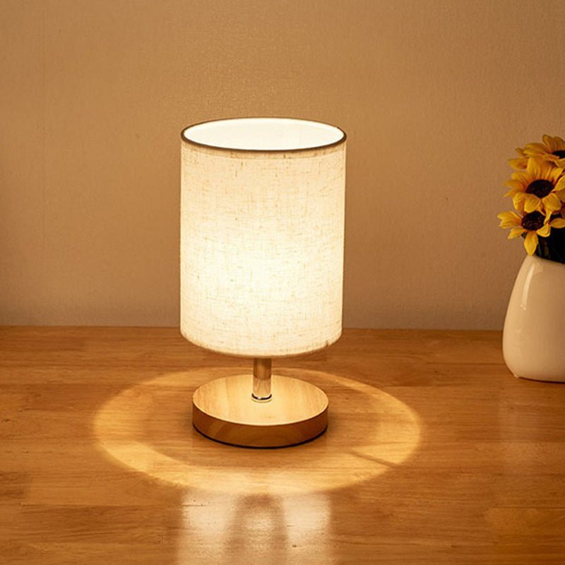 Modern table lamp with beige fabric shade on wooden base, illuminating a warm glow. Ideal for bedroom or living room decor. Cozy lighting accessory.