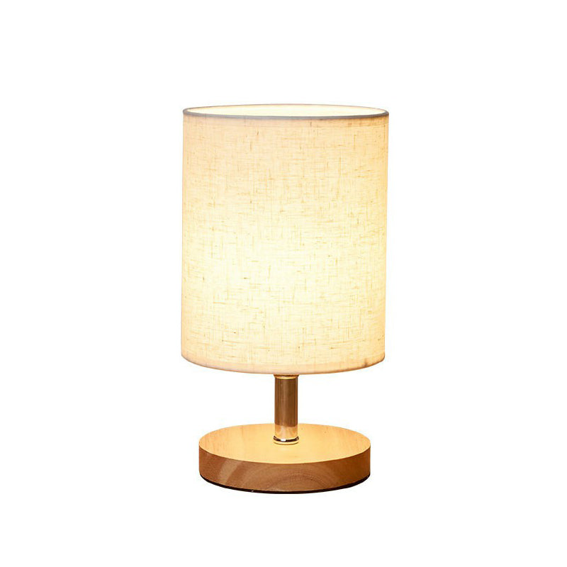 Modern table lamp with cylindrical fabric shade and wooden base, ideal for bedroom or living room decor. Warm ambient lighting.