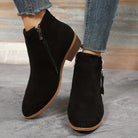 Black suede ankle boots with side zippers, worn with distressed denim jeans. Stylish women's footwear, perfect for casual and trendy outfits.