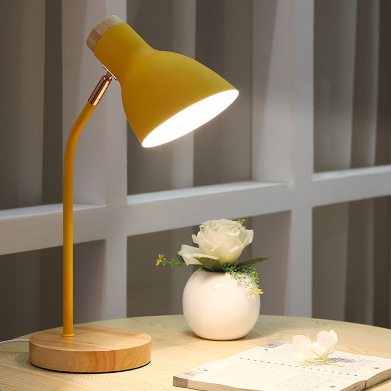 Yellow desk lamp with wooden base illuminating a table with a white rose in a vase and a notepad, perfect for modern home office decor.