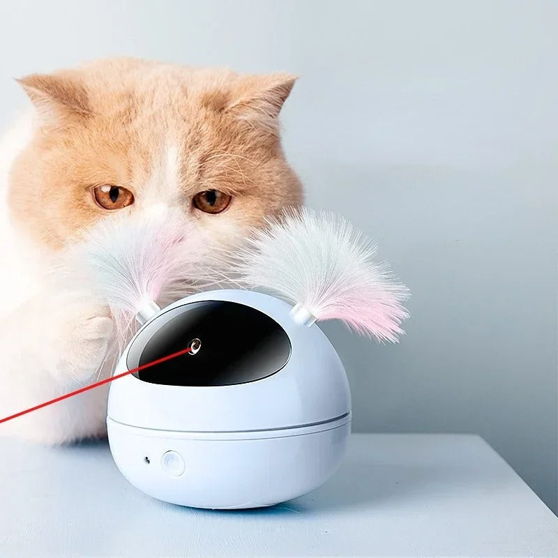 Cat playing with interactive laser toy; fluffy orange cat engaged with white electronic pet toy featuring colorful feather attachments and laser beam.