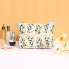 Floral makeup bag with daisy pattern on a white background, surrounded by skincare products and yellow flowers, against a peach backdrop.