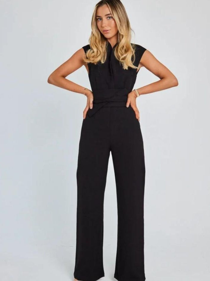 Woman in elegant black jumpsuit with cap sleeves, standing confidently against a plain background. Fashionable women's clothing, stylish outfit.