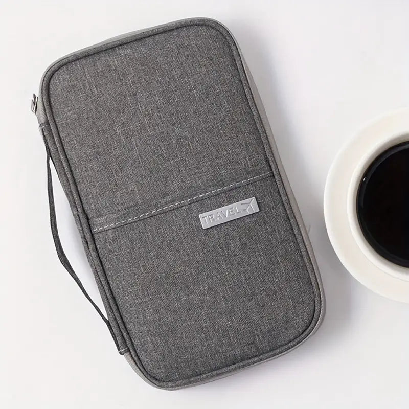 Gray travel wallet organizer with zipper, featuring a sleek design and "TRAVEL" label, placed next to a cup of black coffee on a white surface.