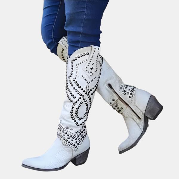 White studded cowboy boots with intricate silver detailing, worn with blue jeans. Stylish western footwear, perfect for fashion-forward cowgirl look.