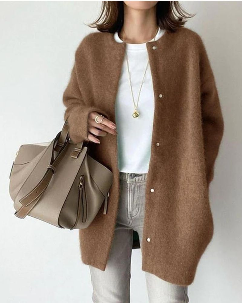 Woman wearing a brown oversized cardigan, white t-shirt, and jeans, holding a beige leather handbag. Fashionable casual outfit with accessories.