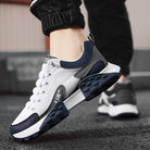 White and navy blue athletic sneakers with textured soles, worn by a person on a street. Stylish, comfortable footwear for running and casual wear.