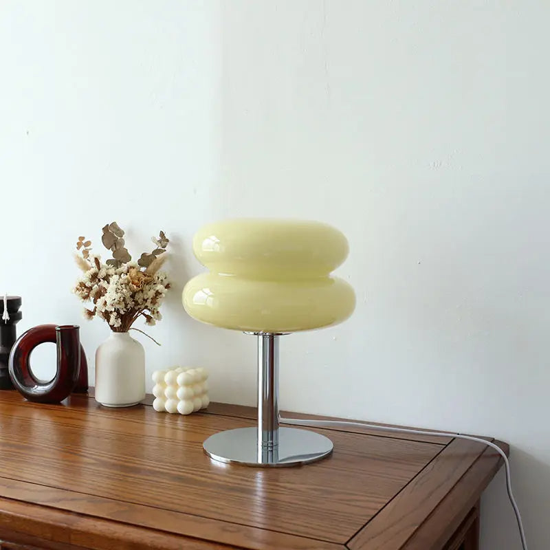 Modern yellow glass table lamp on wooden desk with decorative vases and dried flowers, minimalist home decor, contemporary lighting design.