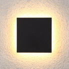 Modern black square LED wall light with warm ambient glow, mounted on textured white surface. Energy-efficient lighting fixture for indoor decor.