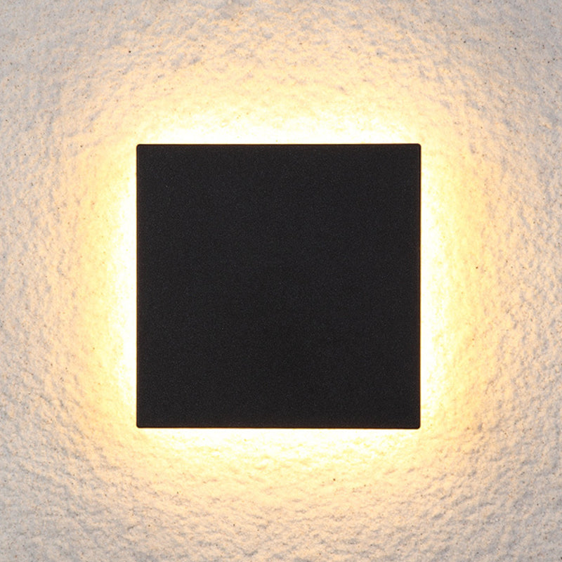 Modern black square LED wall light with warm ambient glow, mounted on textured white surface. Energy-efficient lighting fixture for indoor decor.