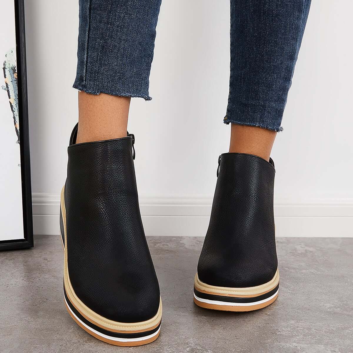 Black leather platform ankle boots with white and tan striped soles, worn with cropped denim jeans. Fashionable women's footwear, modern style.