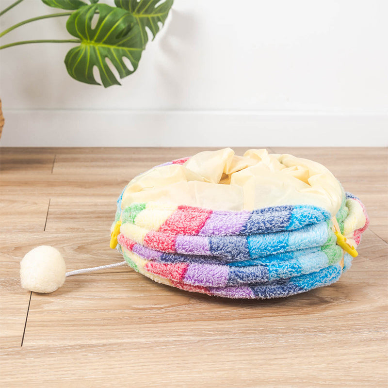 Colorful round cat bed with rainbow pattern and plush pom-pom toy, perfect for pet comfort and playful interaction. Ideal for cozy pet lounging.