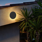 Modern outdoor wall light fixture illuminating a textured wall with tropical plants; energy-efficient LED lighting for stylish exterior decor.