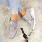 Women's stylish silver sneakers with metallic accents on a fluffy rug, paired with ripped jeans, sunglasses, and a watch. Fashion footwear.