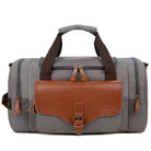 Gray canvas duffel bag with brown leather accents, featuring multiple zippered compartments and a sturdy handle. Ideal for travel and gym use.